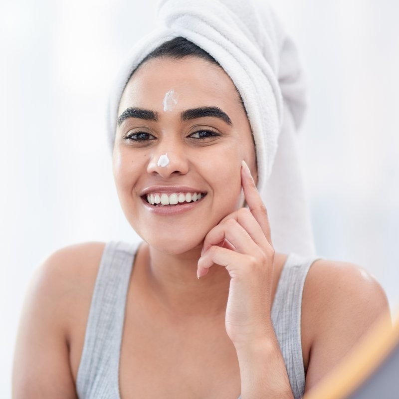 A model with glowing skin gently massages a natural creamy face wash onto her cheek.